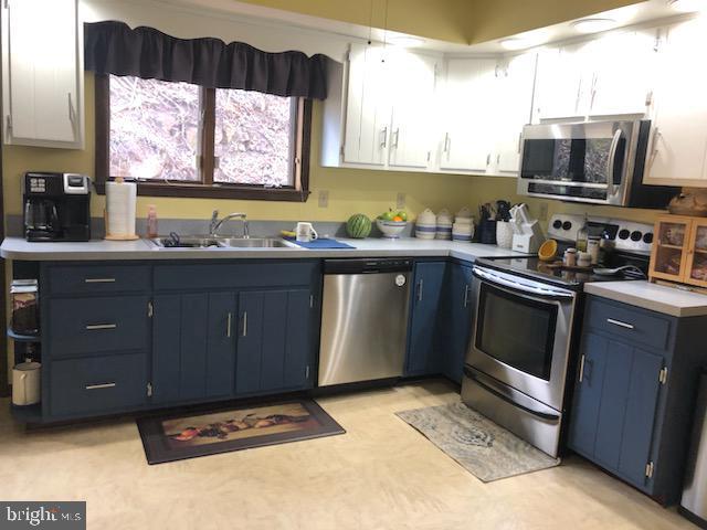 kitchen with light floors, stainless steel appliances, light countertops, a sink, and blue cabinets