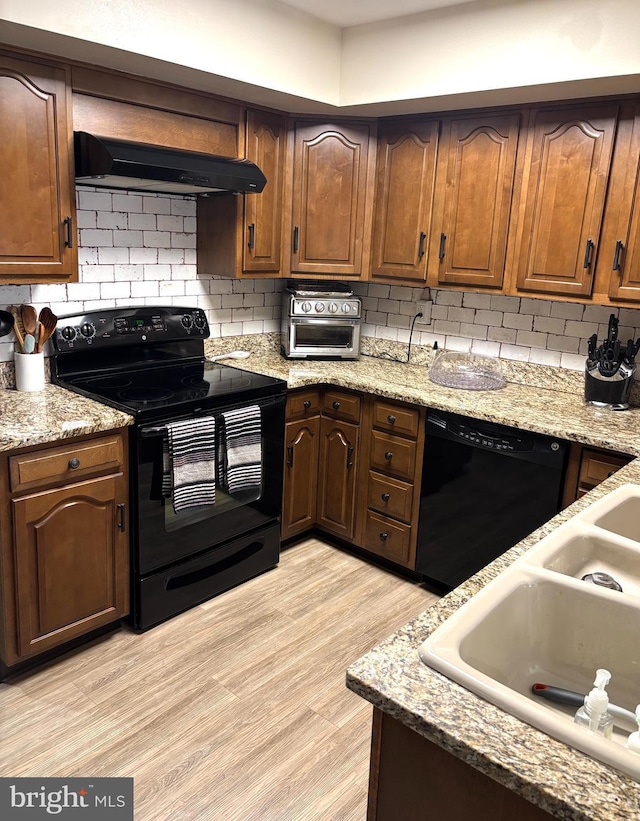 kitchen with light wood finished floors, decorative backsplash, a sink, under cabinet range hood, and black appliances