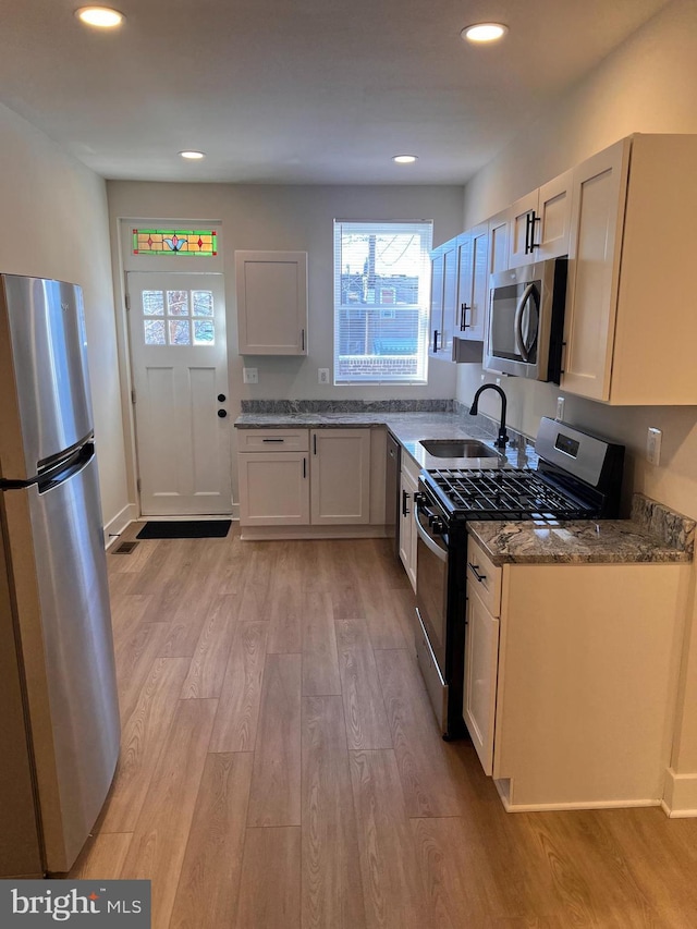 kitchen with dark stone countertops, stainless steel appliances, light wood-type flooring, a sink, and recessed lighting