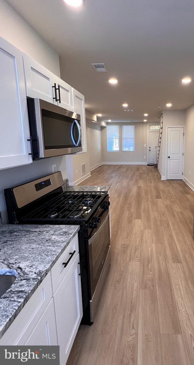 kitchen featuring recessed lighting, white cabinets, appliances with stainless steel finishes, light wood-type flooring, and light stone countertops