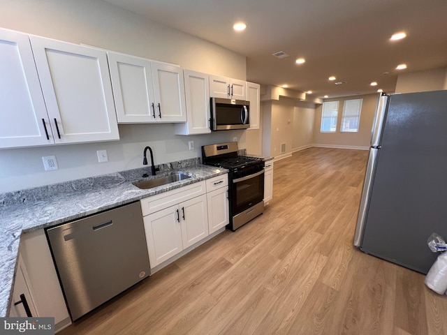 kitchen featuring white cabinets, light wood-style flooring, appliances with stainless steel finishes, a sink, and recessed lighting