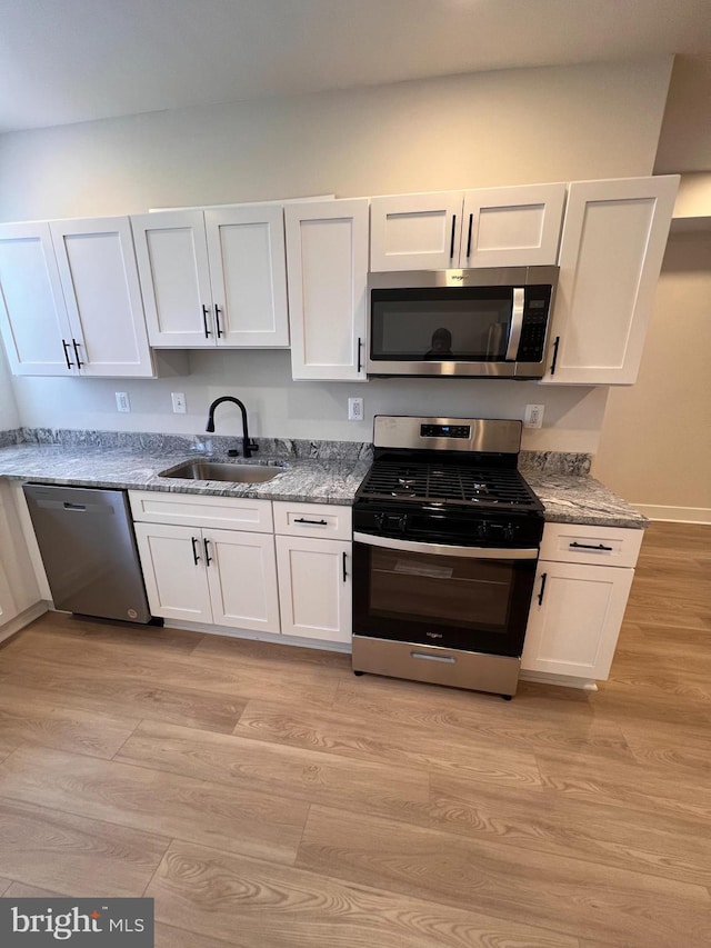 kitchen with white cabinets, light stone countertops, stainless steel appliances, light wood-type flooring, and a sink