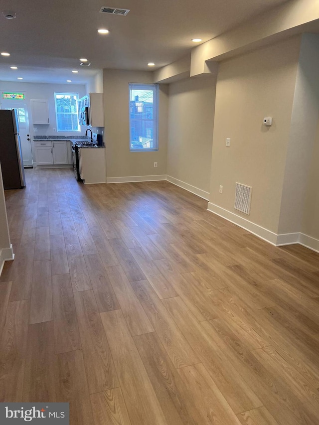 unfurnished living room featuring light wood-type flooring, baseboards, and visible vents