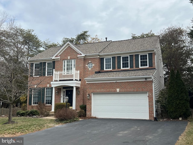 colonial inspired home featuring aphalt driveway, an attached garage, and brick siding