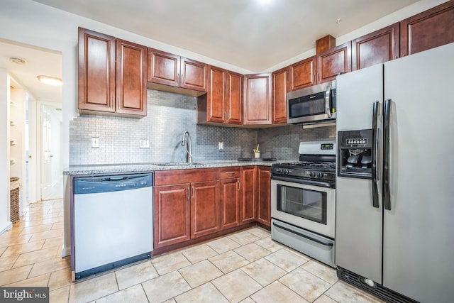 kitchen with appliances with stainless steel finishes, a sink, decorative backsplash, and light stone countertops