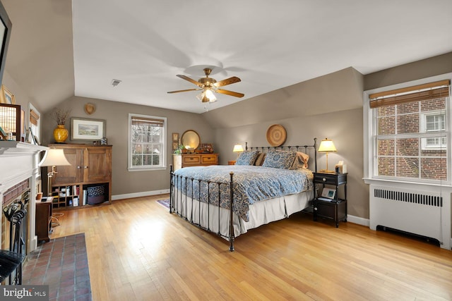 bedroom featuring a fireplace, radiator, visible vents, vaulted ceiling, and light wood-type flooring