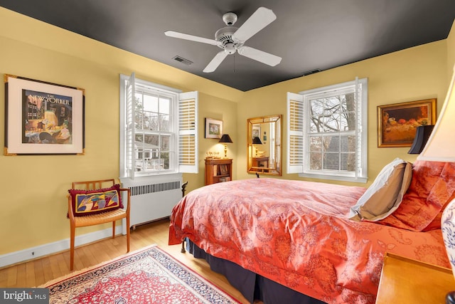 bedroom featuring radiator heating unit, multiple windows, visible vents, and light wood-style flooring