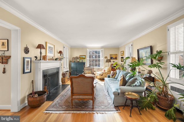 living area featuring crown molding, a fireplace with raised hearth, baseboards, and light wood-style floors