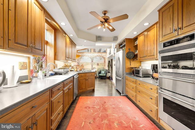 kitchen featuring wood finished floors, a sink, light countertops, appliances with stainless steel finishes, and brown cabinetry