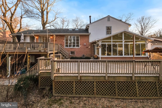 back of property with brick siding, a sunroom, and a wooden deck