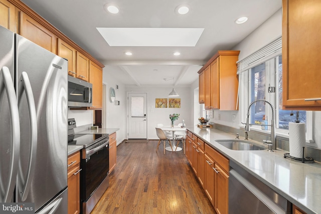 kitchen with a skylight, dark wood-style flooring, a sink, appliances with stainless steel finishes, and brown cabinets