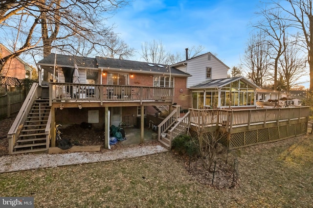 back of house with a sunroom, a shingled roof, stairs, a deck, and brick siding