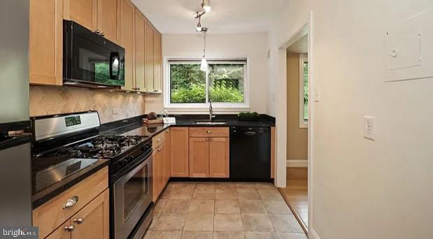 kitchen featuring light tile patterned floors, a sink, backsplash, black appliances, and dark countertops