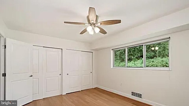 unfurnished bedroom with a ceiling fan, baseboards, visible vents, light wood-style floors, and two closets