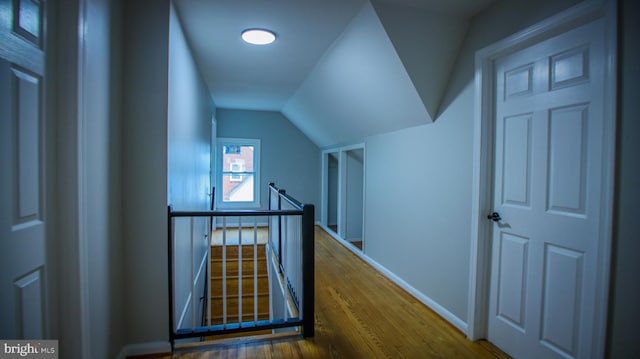 hallway with an upstairs landing, baseboards, lofted ceiling, and wood finished floors