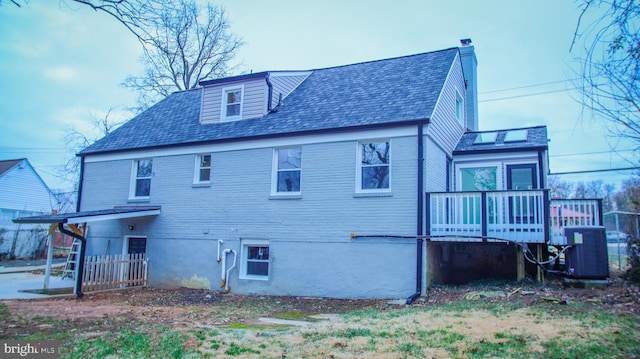 rear view of house featuring cooling unit, roof with shingles, a wooden deck, and a chimney