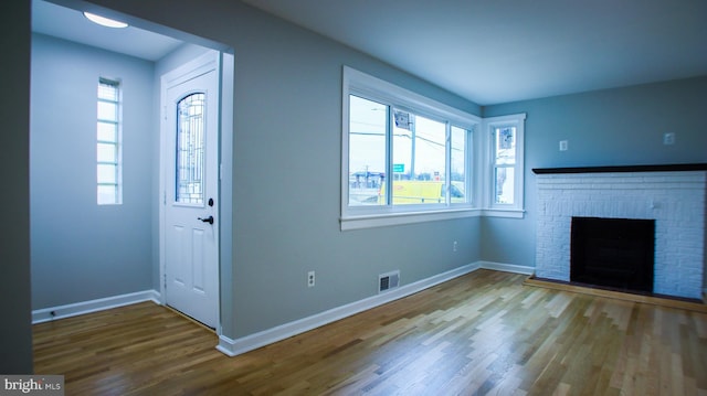 foyer entrance featuring wood finished floors, a fireplace, baseboards, and visible vents