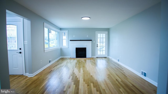 unfurnished living room with a brick fireplace, plenty of natural light, and visible vents