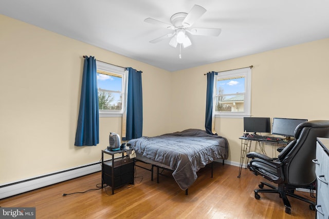 bedroom with baseboard heating, multiple windows, light wood-type flooring, and baseboards