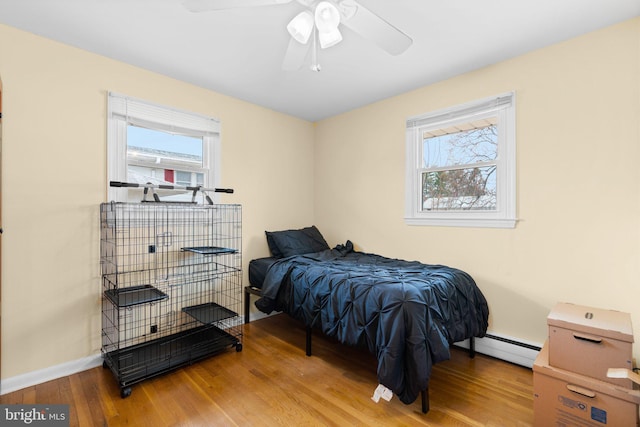 bedroom with a baseboard radiator, baseboards, hardwood / wood-style floors, and a ceiling fan