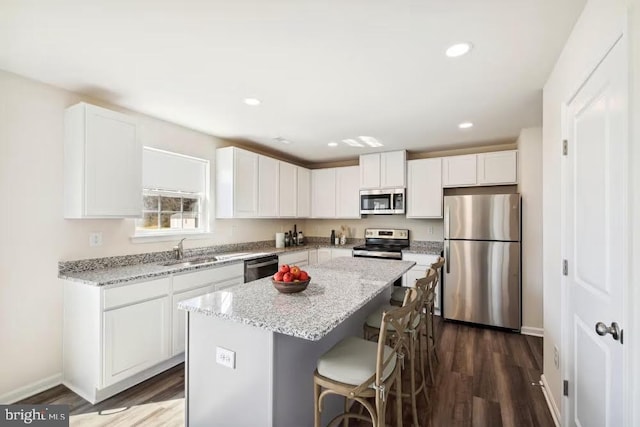 kitchen with appliances with stainless steel finishes, a kitchen island, light stone counters, and white cabinetry