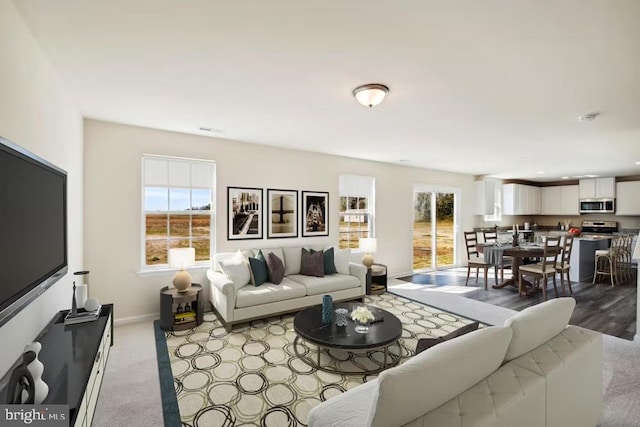 living area featuring baseboards, light carpet, visible vents, and a healthy amount of sunlight