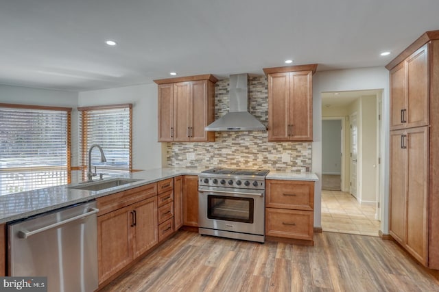 kitchen featuring stainless steel appliances, light wood-style flooring, decorative backsplash, a sink, and wall chimney exhaust hood