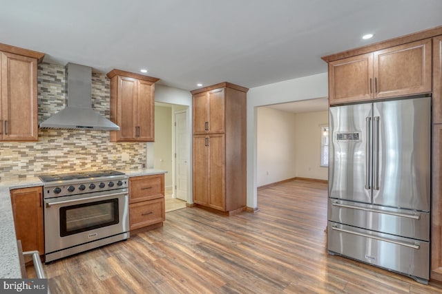 kitchen featuring baseboards, light wood-style floors, appliances with stainless steel finishes, wall chimney range hood, and decorative backsplash