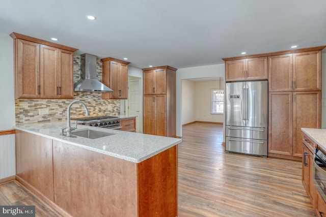 kitchen featuring wall chimney exhaust hood, appliances with stainless steel finishes, light wood-style flooring, and a sink