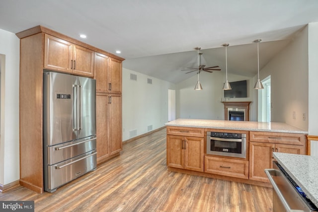 kitchen featuring a glass covered fireplace, ceiling fan, vaulted ceiling, stainless steel appliances, and light wood-style floors