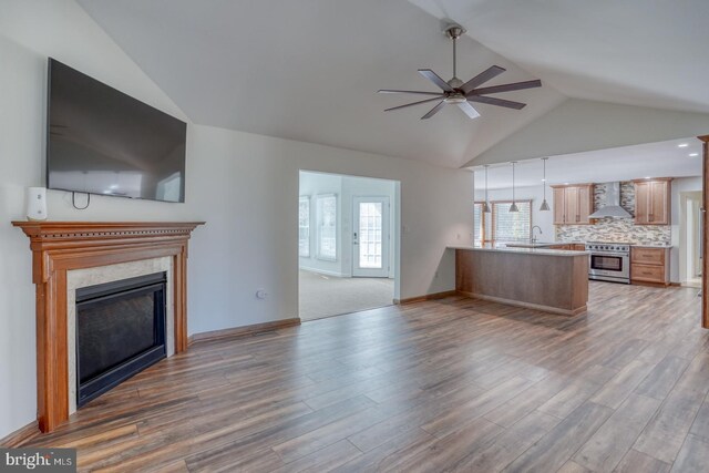 unfurnished living room featuring a sink, ceiling fan, a fireplace, and wood finished floors