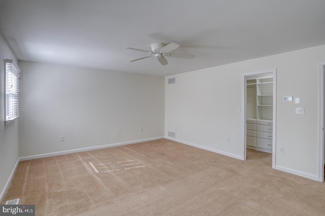 unfurnished bedroom with light colored carpet, visible vents, baseboards, a closet, and a walk in closet