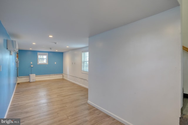 spare room with light wood-style floors, baseboards, an AC wall unit, and recessed lighting