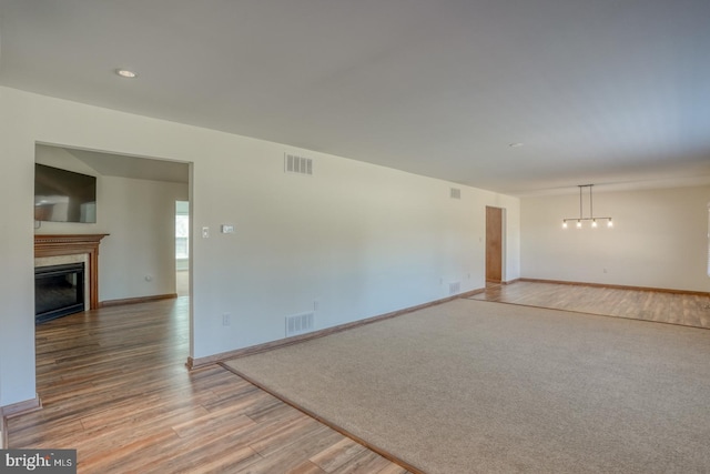 empty room with a glass covered fireplace, baseboards, visible vents, and light wood finished floors