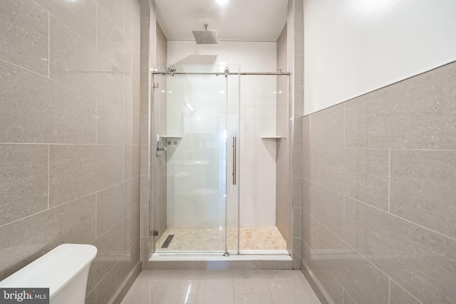 full bath with tile walls, a shower stall, toilet, and tile patterned floors