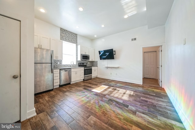 kitchen with white cabinets, appliances with stainless steel finishes, dark wood-type flooring, light countertops, and backsplash