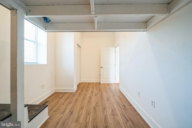 empty room with light wood-type flooring, baseboards, and beam ceiling