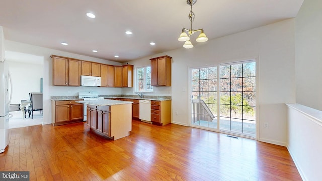 kitchen featuring white appliances, a kitchen island, visible vents, light stone countertops, and pendant lighting