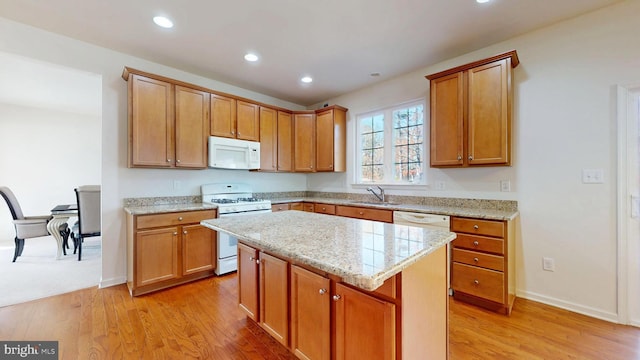 kitchen with a center island, brown cabinets, light wood finished floors, a sink, and white appliances