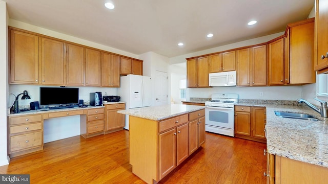 kitchen with built in desk, a kitchen island, a sink, light stone countertops, and white appliances