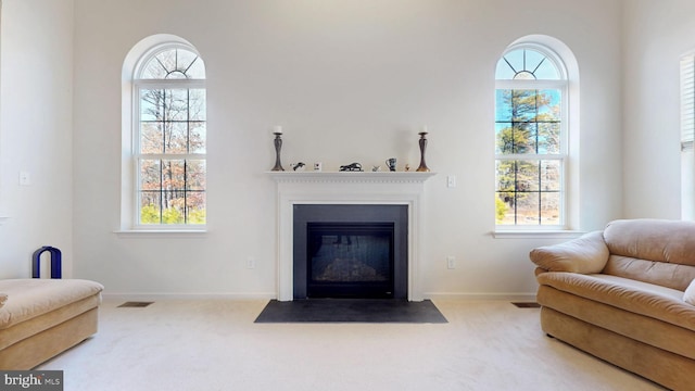 living area featuring a fireplace with flush hearth, visible vents, light carpet, and baseboards