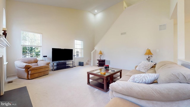 carpeted living area featuring visible vents, a high ceiling, and stairs