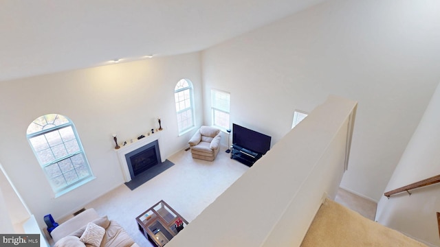 living room featuring a fireplace with flush hearth, a towering ceiling, and light colored carpet