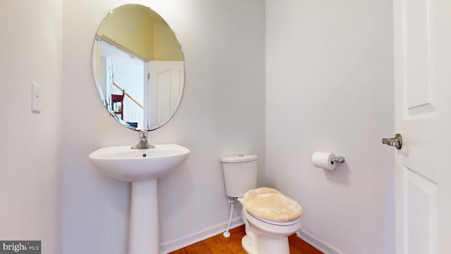 half bath with baseboards, a sink, toilet, and wood finished floors