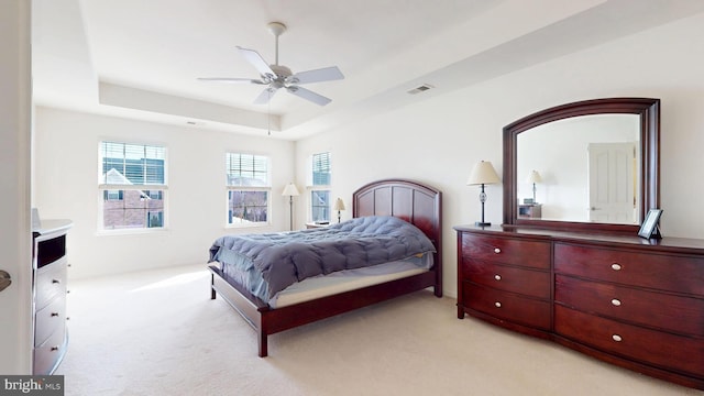 bedroom with light colored carpet, a raised ceiling, visible vents, and ceiling fan