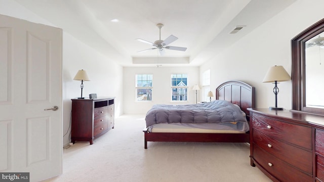 bedroom featuring a ceiling fan, visible vents, a tray ceiling, and light colored carpet