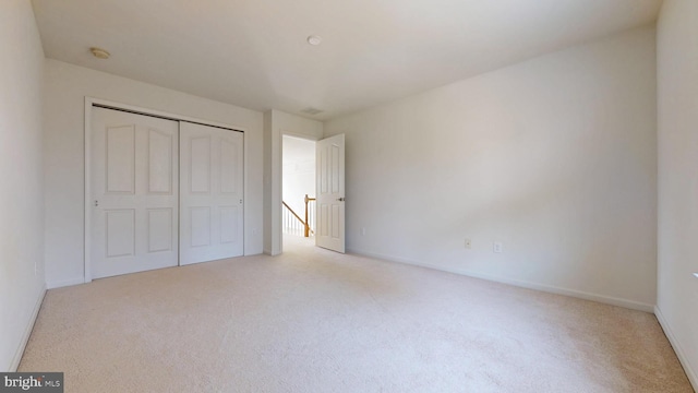 unfurnished bedroom featuring light carpet, a closet, and baseboards