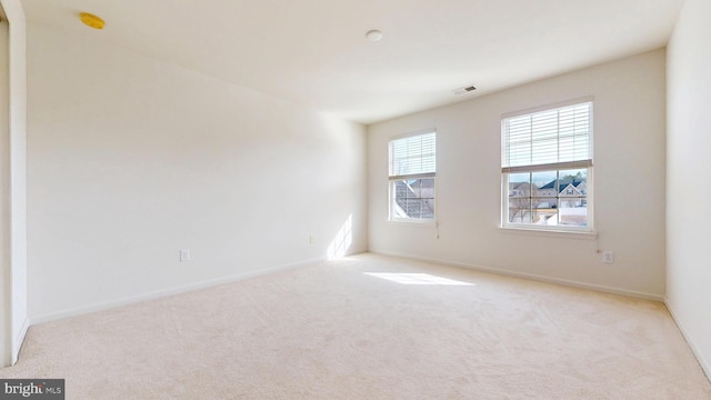 empty room featuring baseboards, visible vents, and light colored carpet