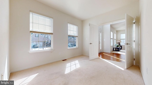 unfurnished bedroom with baseboards, multiple windows, visible vents, and light colored carpet