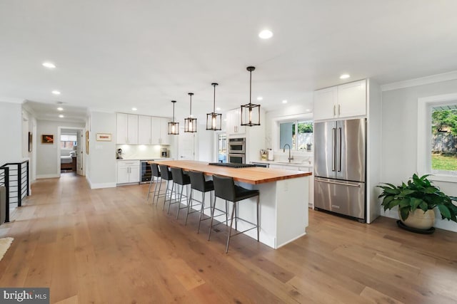 kitchen with a breakfast bar area, beverage cooler, wooden counters, a kitchen island, and appliances with stainless steel finishes